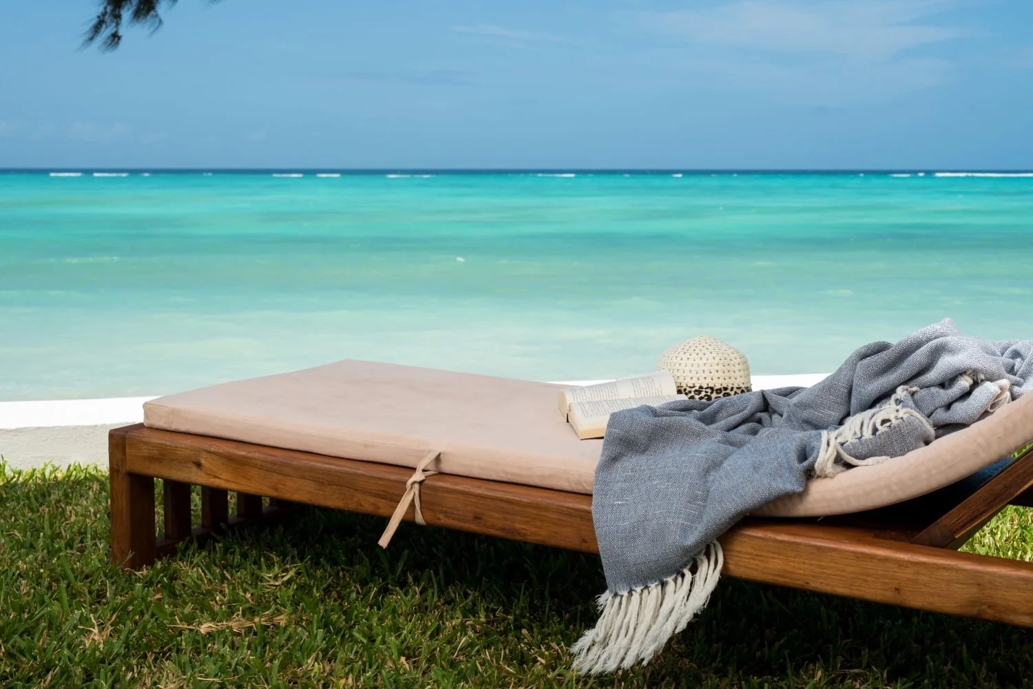 Comfortable wooden sun lounger with soft cushions overlooking turquoise water.
