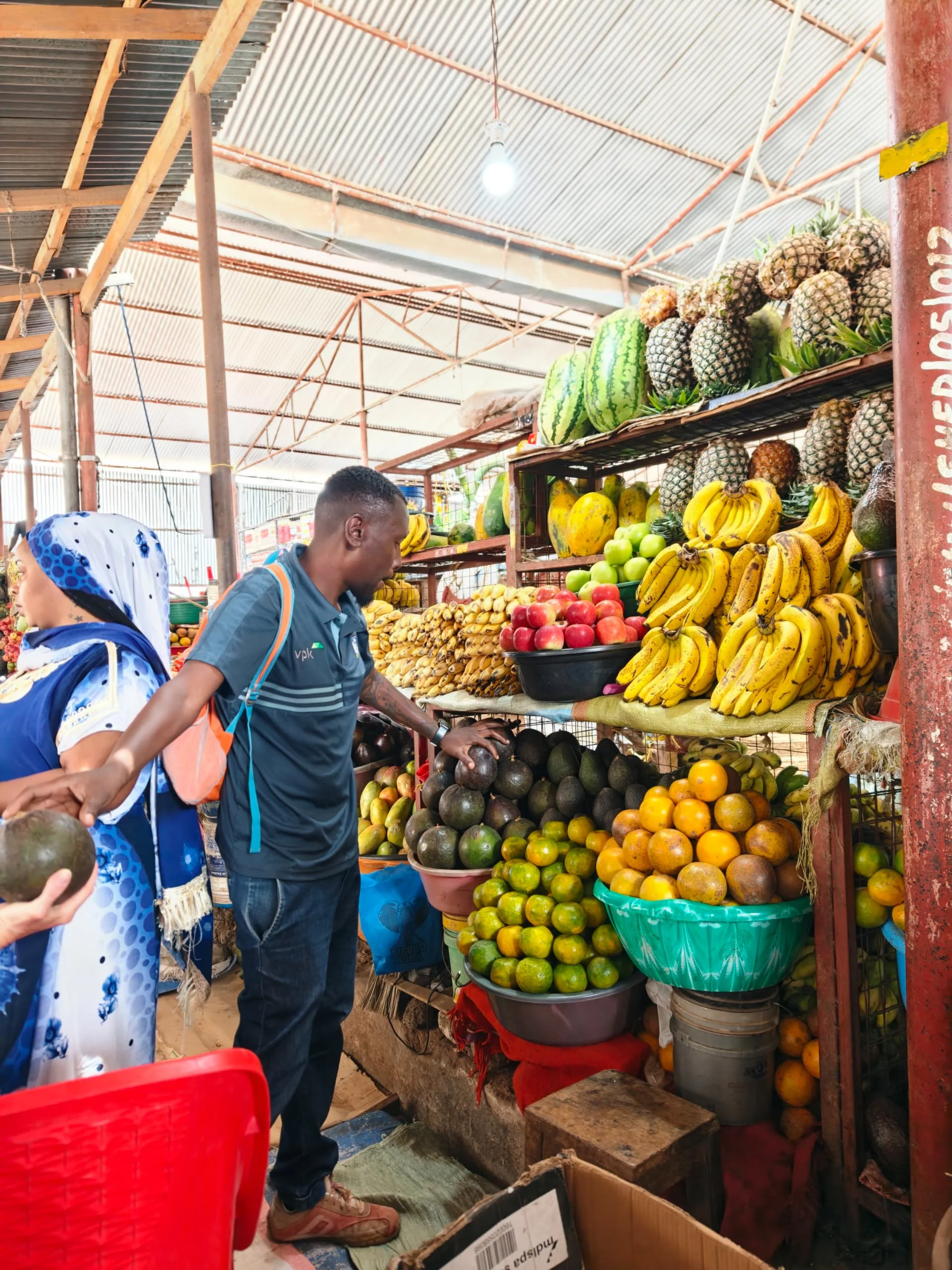 Market vendor arranging fresh bananas and tropical fruits at a produce stall in Arusha Central Market.