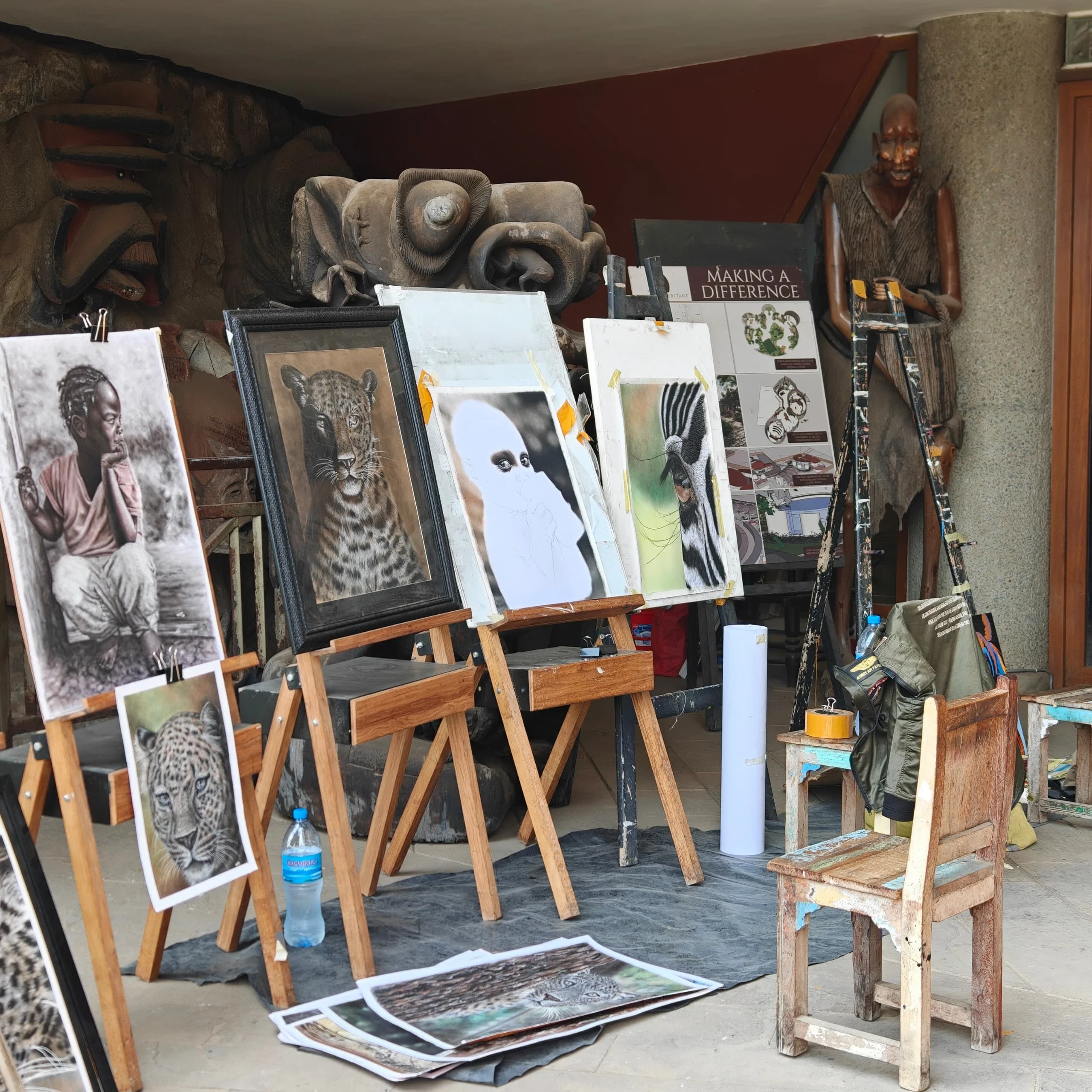 Art gallery workspace at Cultural Heritage Centre Arusha displaying paintings on easels and wooden sculptures.