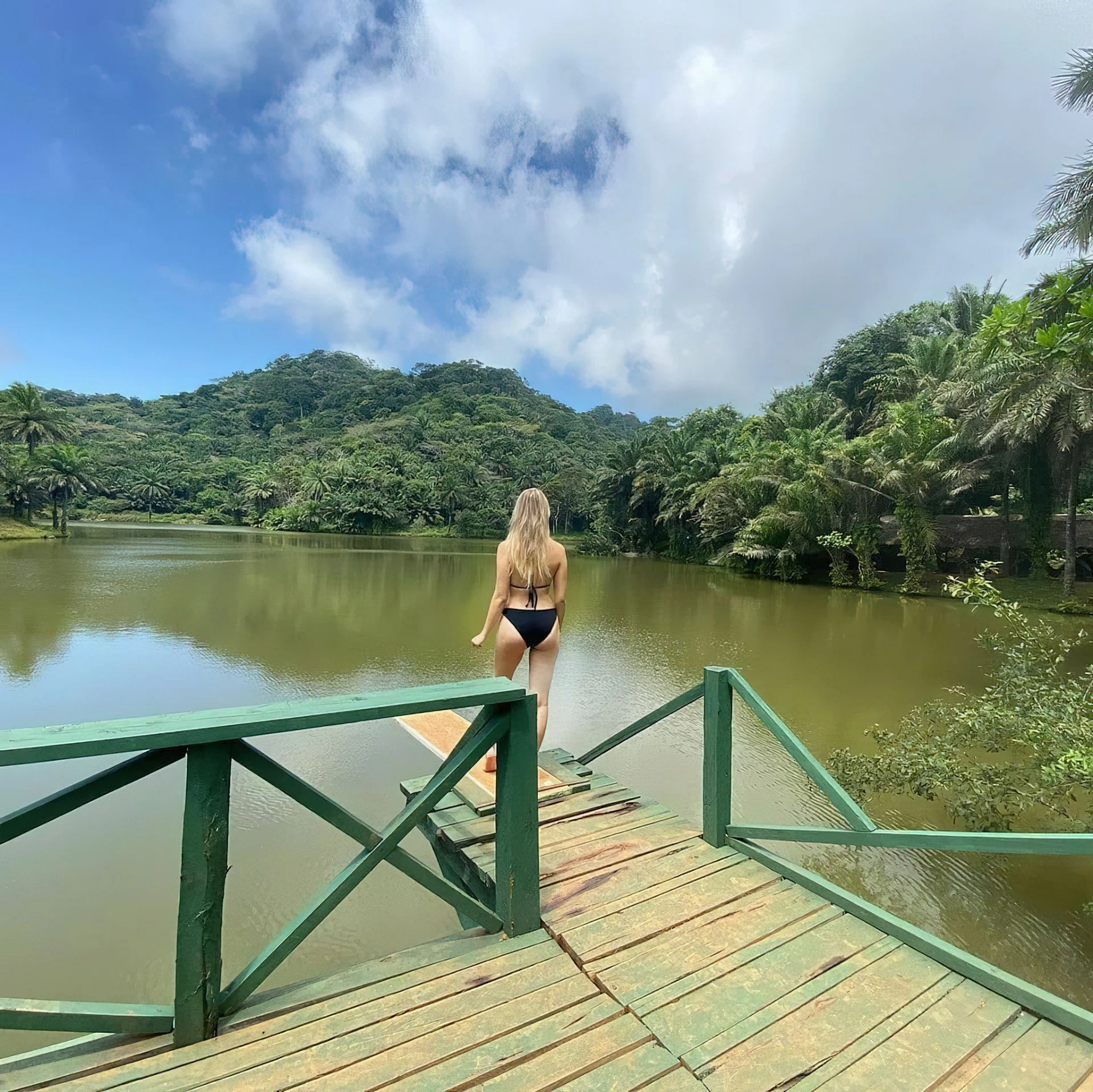 Tourist walking across a green wooden bridge over a tranquil lake in Magoroto Forest.