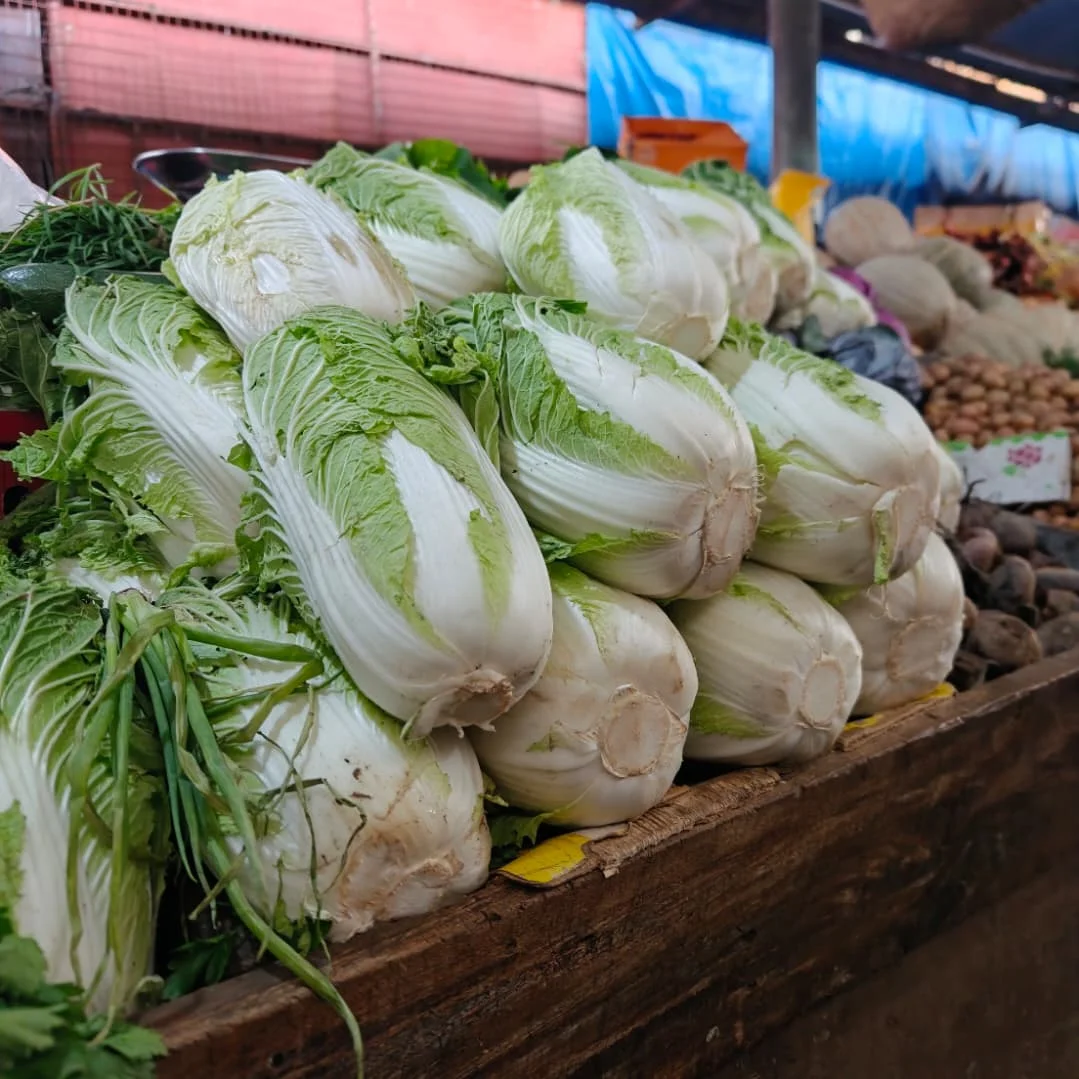 Stack of fresh napa cabbages displayed on a wooden stall at Arusha Central Market.