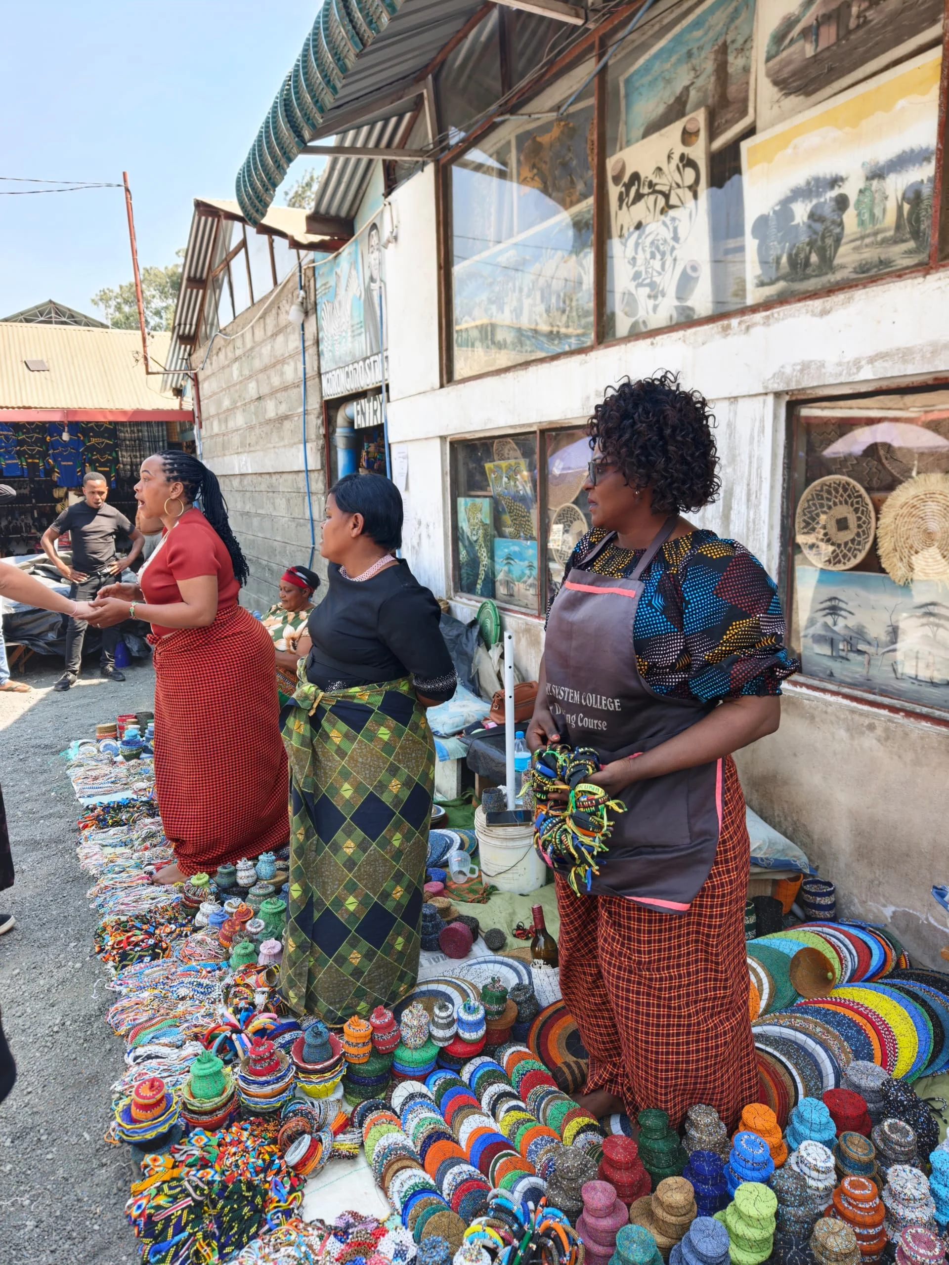 Maasai women selling colorful beaded bowls and crafts at an outdoor market stall in Arusha.