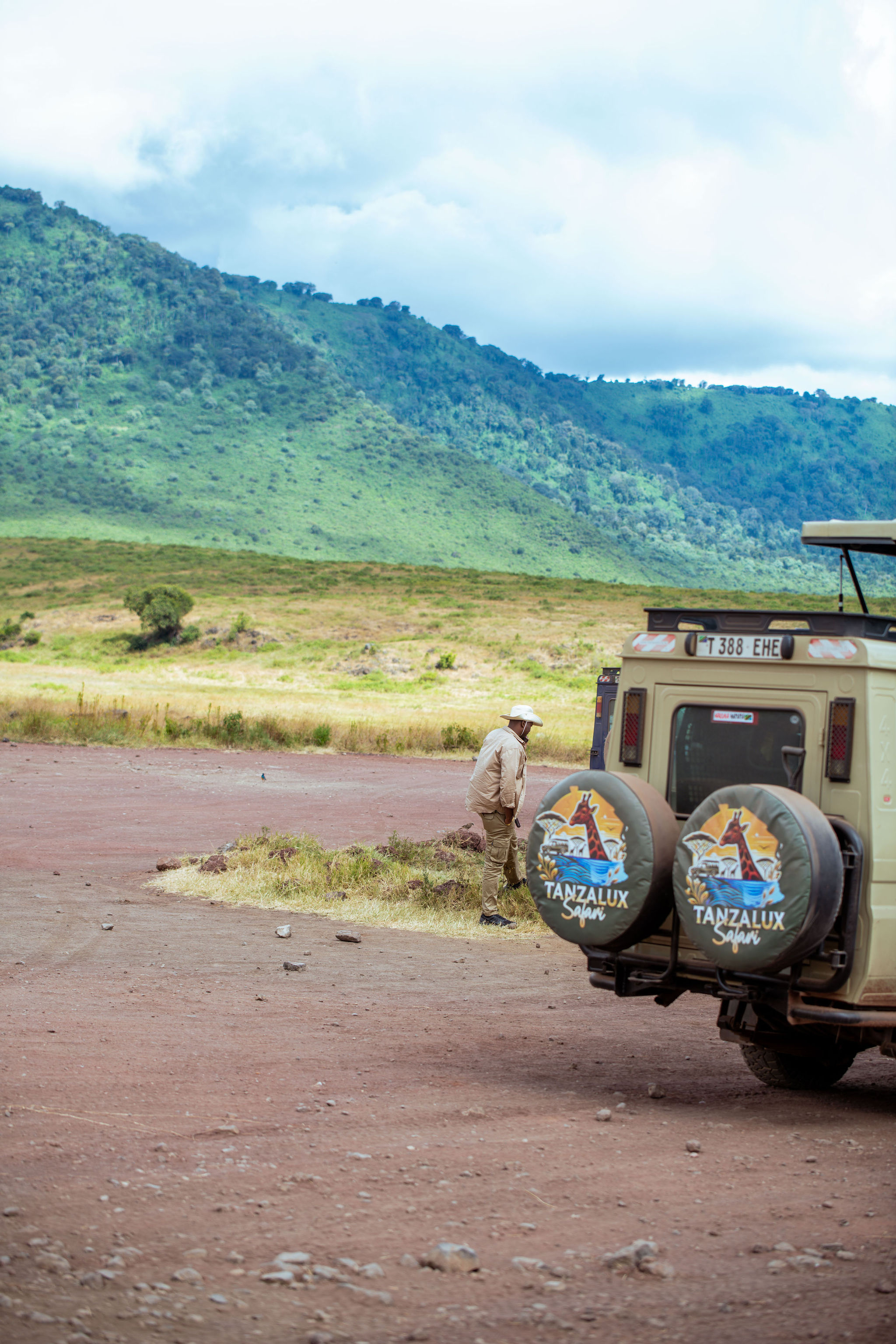 A 4x4 safari Land Cruiser driving on a dirt road through the green Ngorongoro Crater valley.