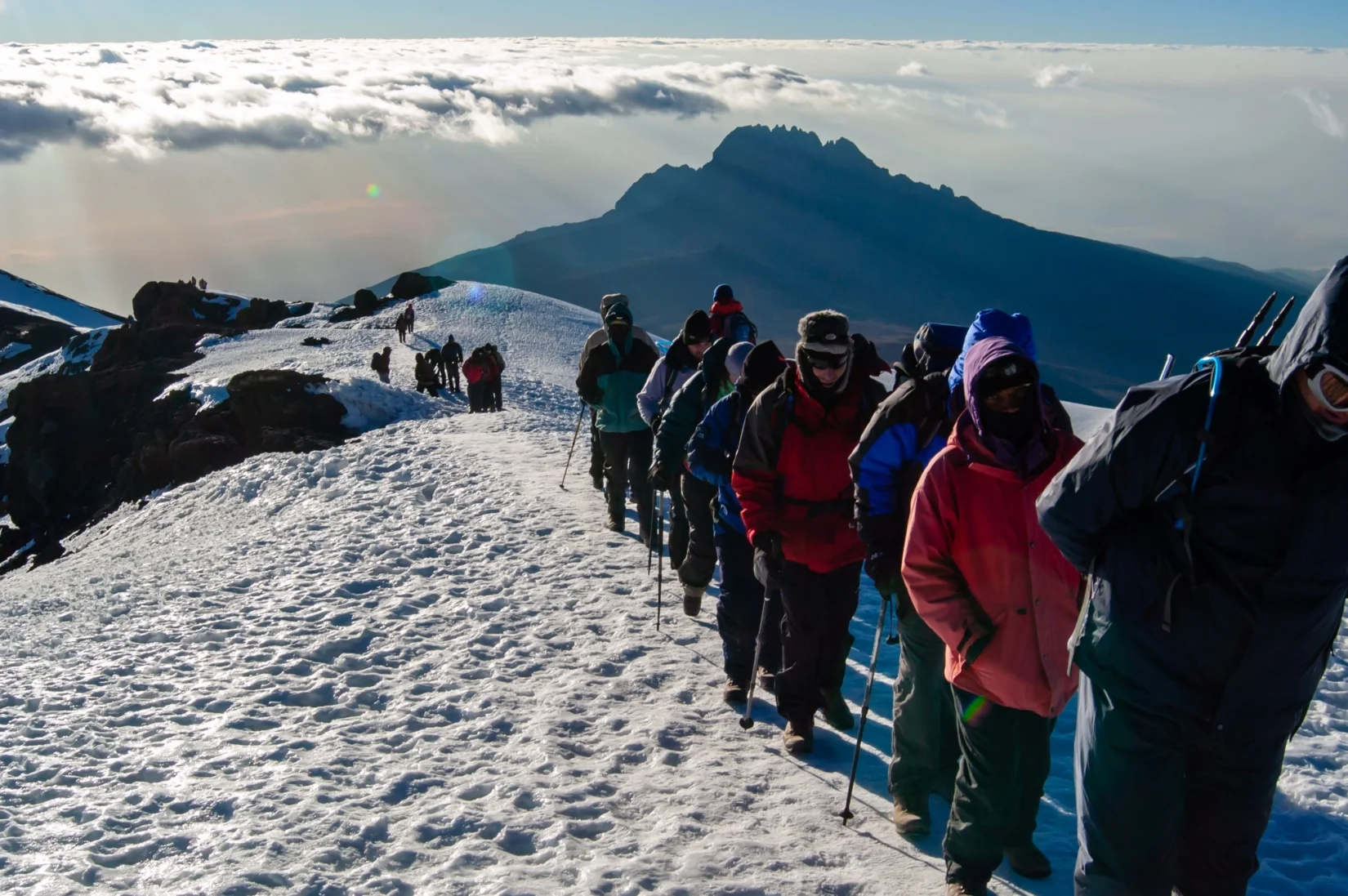 Line of climbers in thermal jackets hiking up a snowy mountain trail on Mount Kilimanjaro, Tanzania.