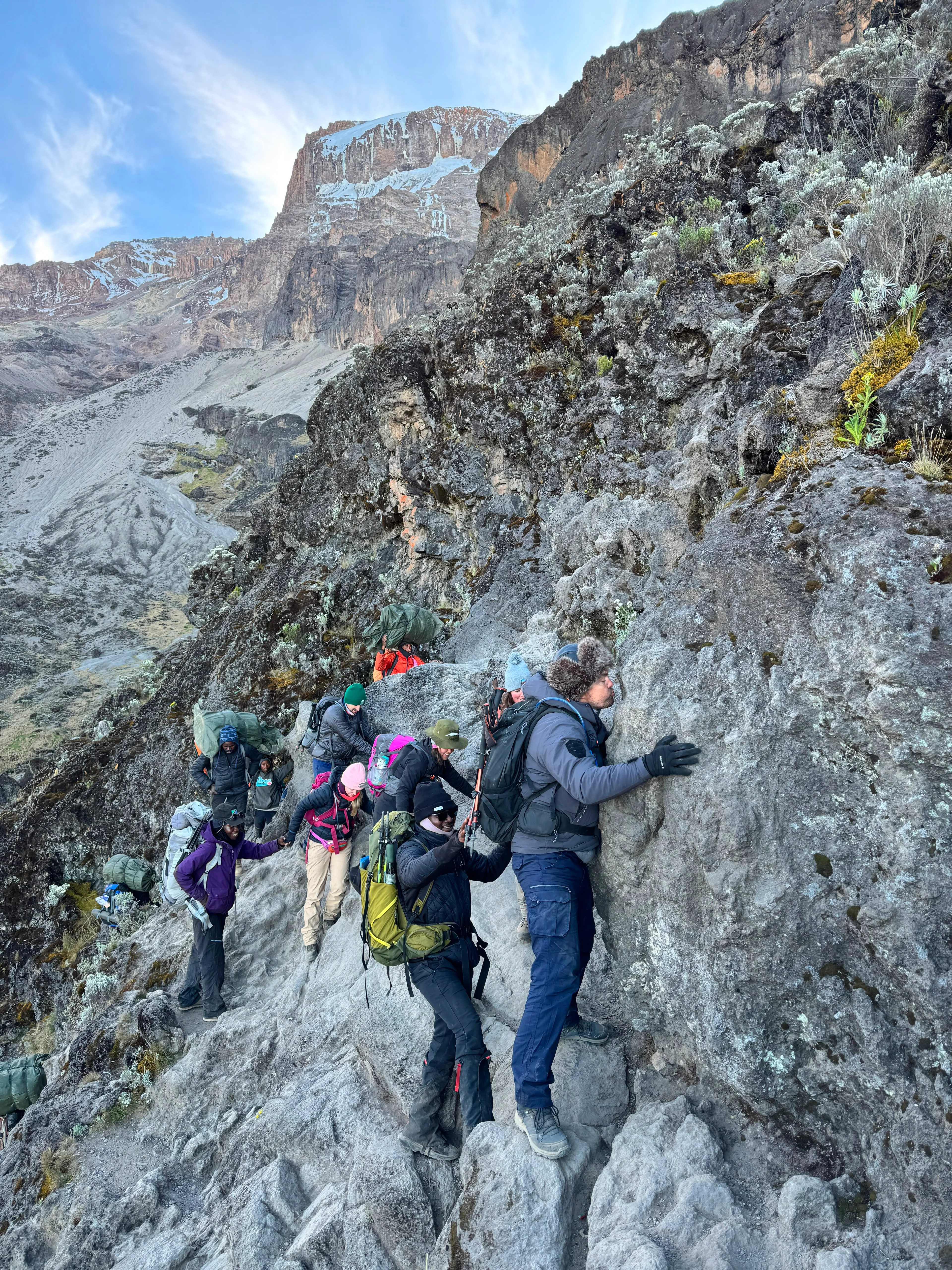 Hikers traverse a narrow rocky section of Mount Kilimanjaro, navigating steep volcanic cliffs on a challenging Tanzania trek.