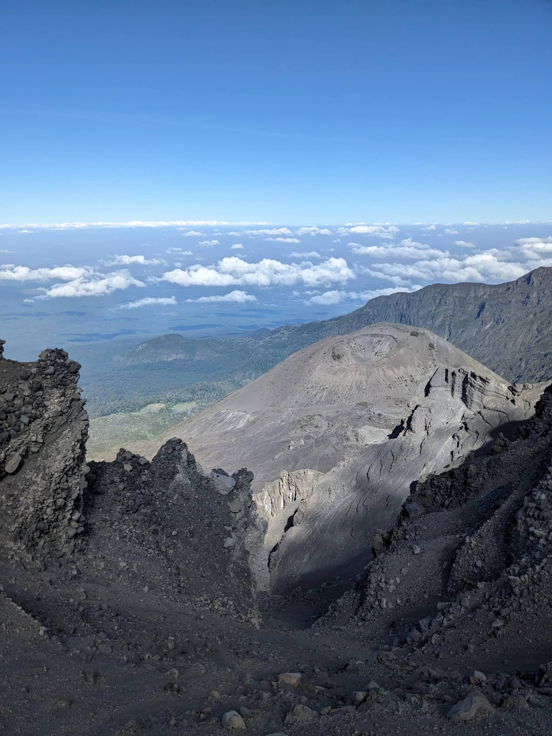 Rugged volcanic slopes on Mount Kilimanjaro overlook distant valleys and clouds during a high-altitude Tanzania trekking day.