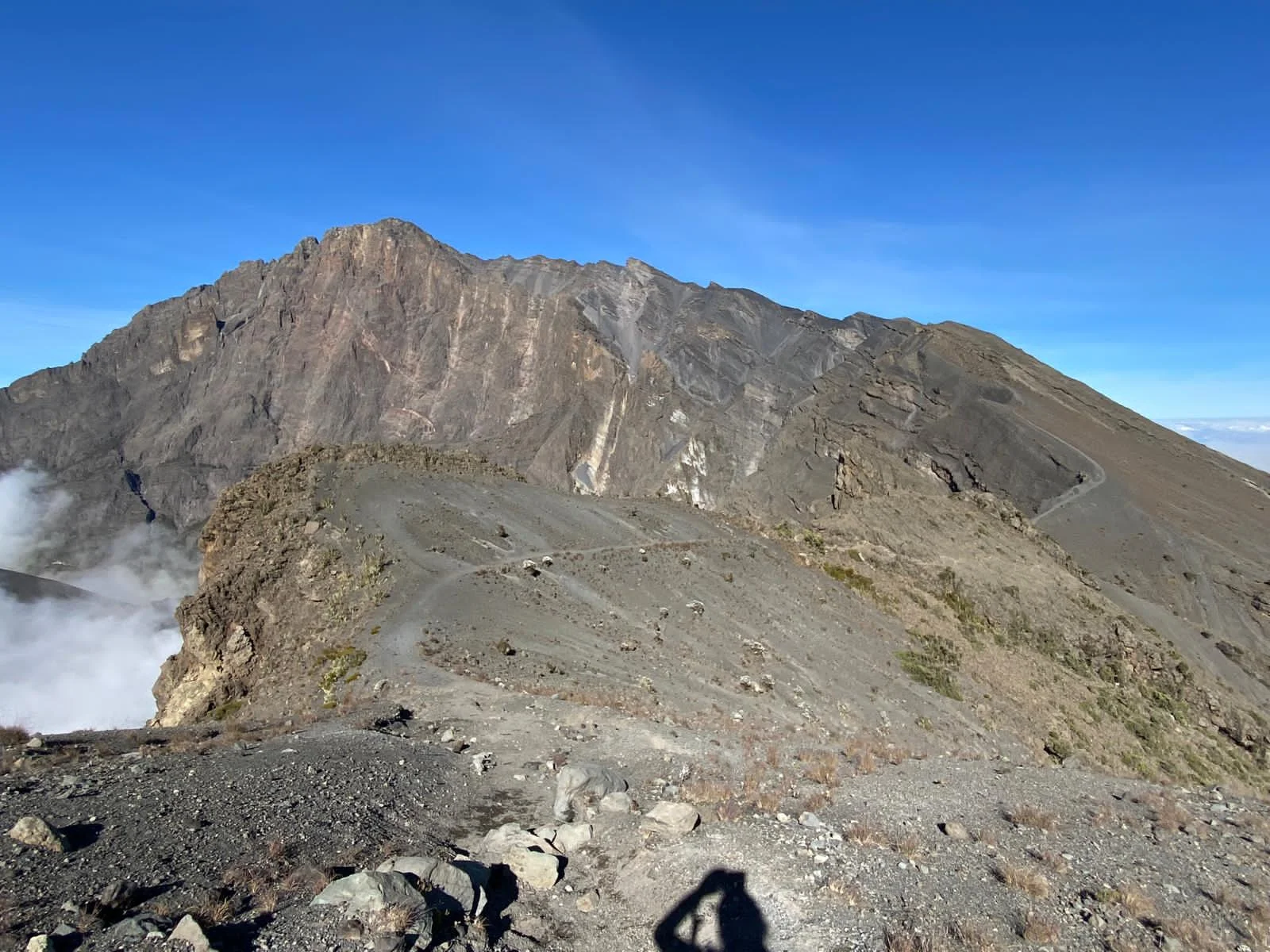 Rocky alpine desert trail looking towards volcanic mountain peaks under clear blue sky on Mount Kilimanjaro.