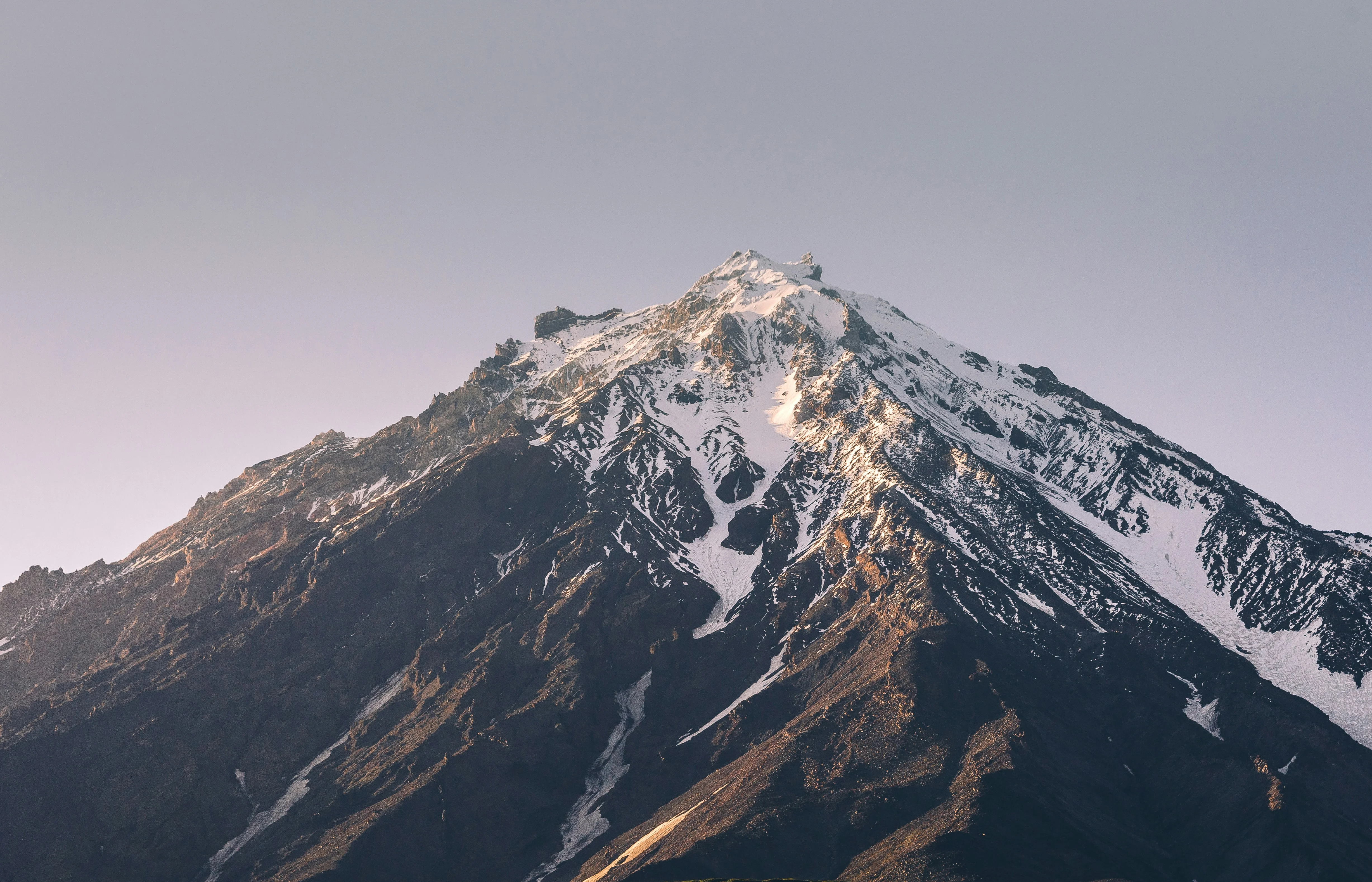 Snow-dusted peak of Mount Kilimanjaro rises above dark volcanic slopes along Tanzania's scenic Lemosho Route trekking trails.