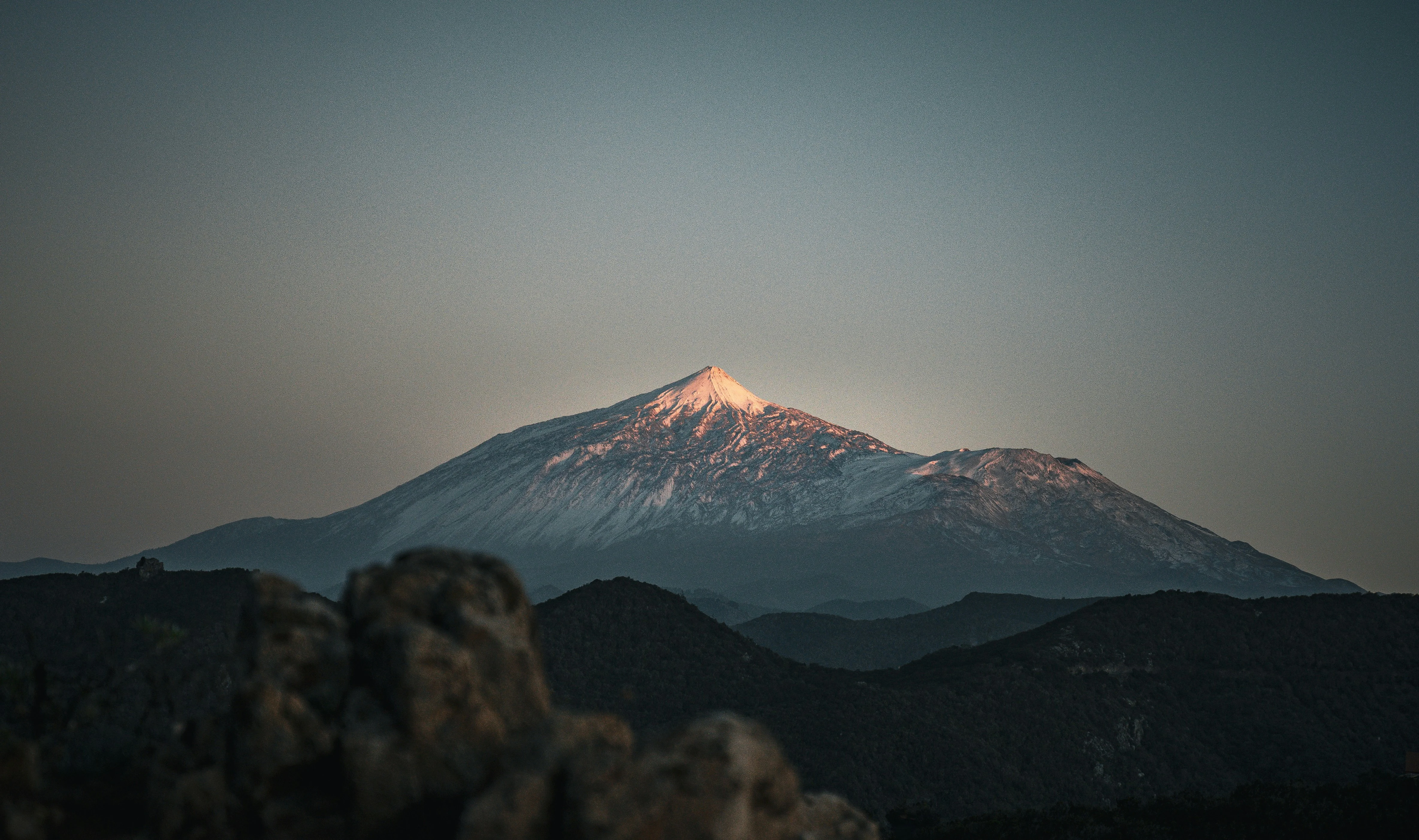 Mount Kilimanjaro shines at sunrise above rugged volcanic ridges, with its snow-covered summit beneath a clear Tanzanian sky.