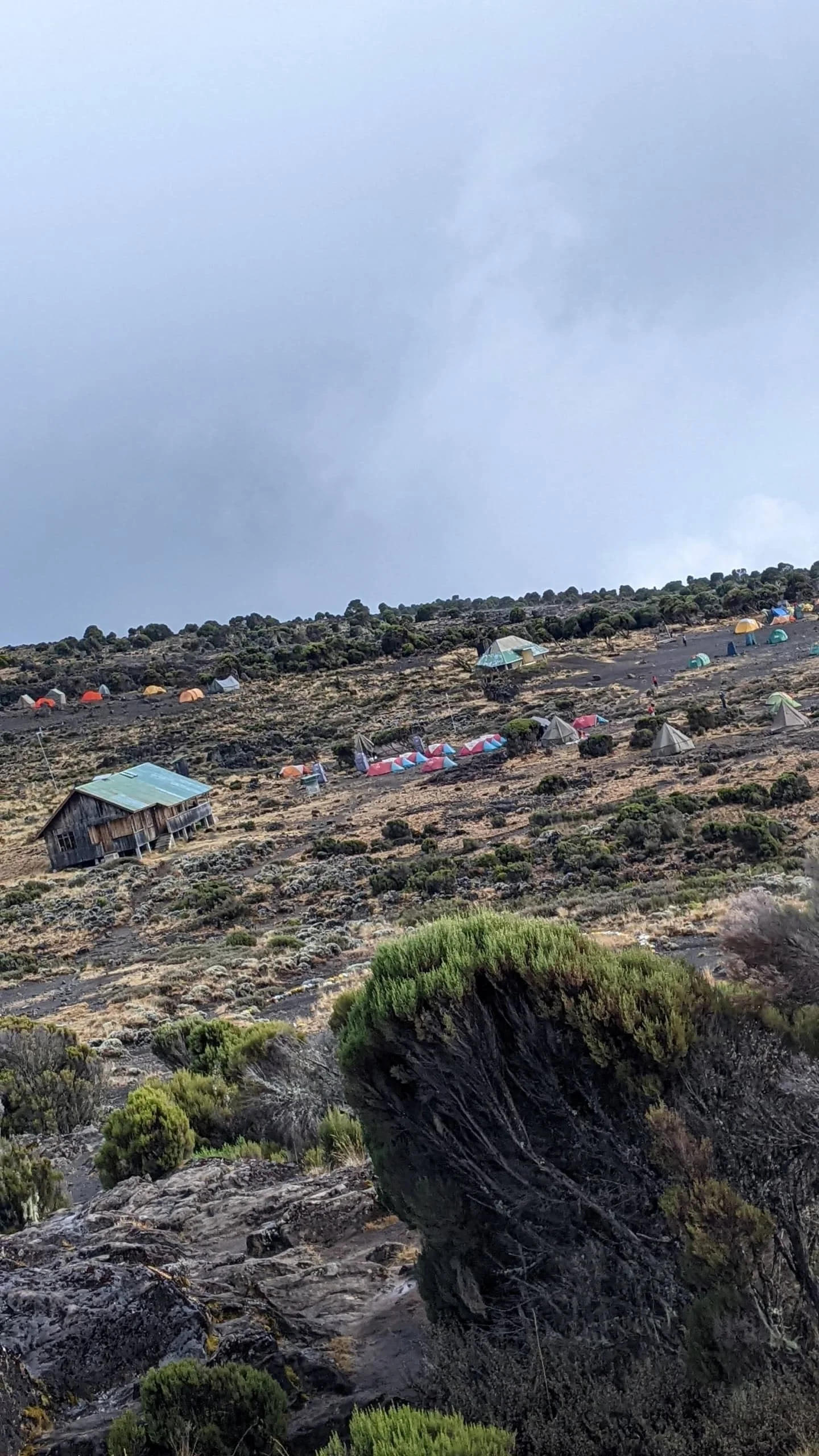 Mount Kilimanjaro campsite with colorful tents set across rocky alpine terrain beneath cloudy skies during the Tanzania trek.