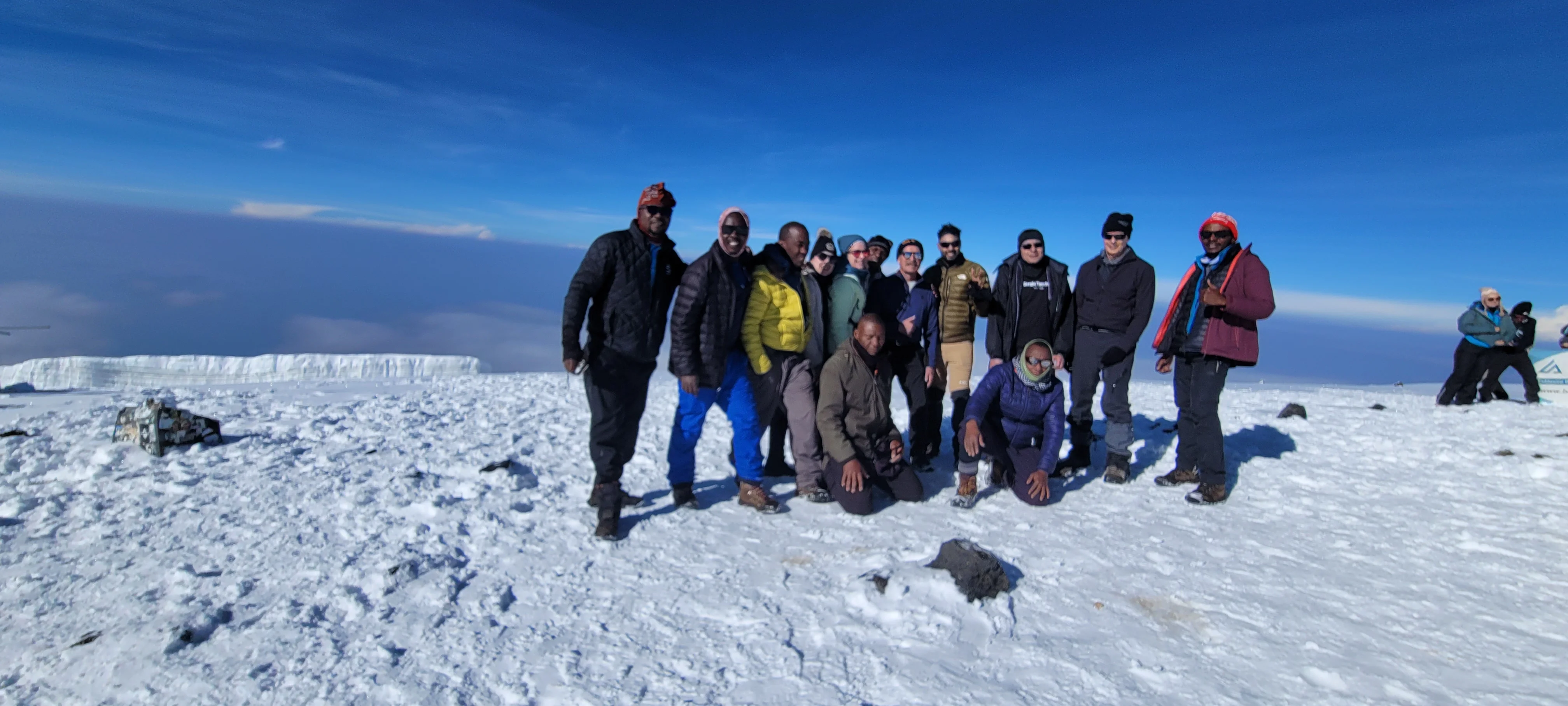 Trekkers celebrate together on Mount Kilimanjaro's snowy summit plateau beneath a vivid blue sky after their demanding climb.