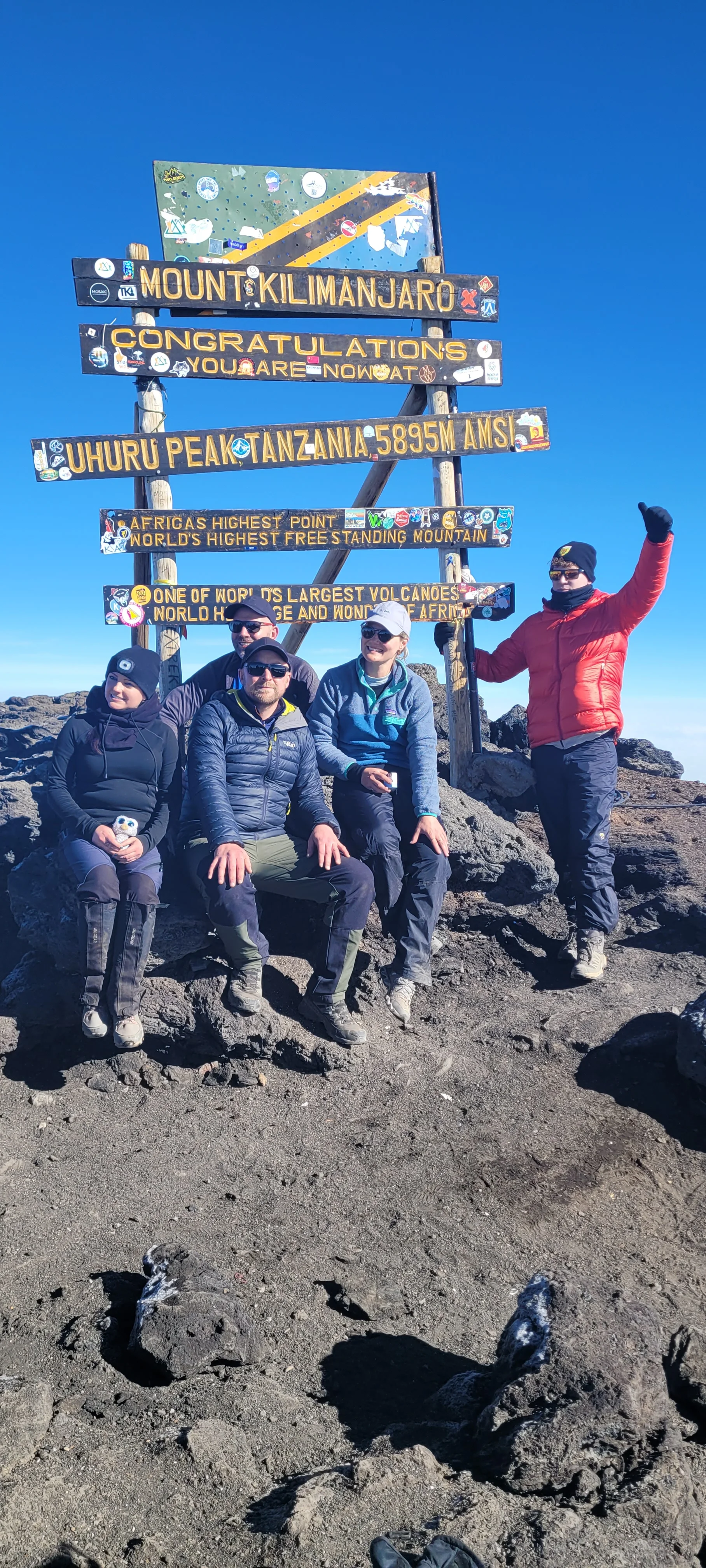 Trekkers celebrate at Uhuru Peak on Mount Kilimanjaro beneath the summit sign after completing a demanding climb in Tanzania.
