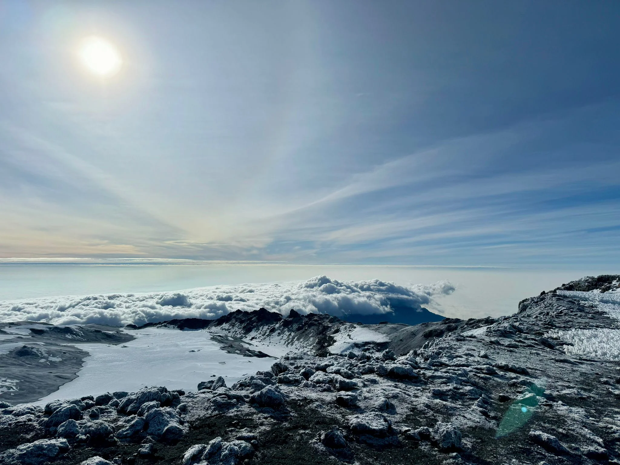 Bright sun shining over snow-capped summit glaciers and crater rim above cloud cover on Mount Kilimanjaro.