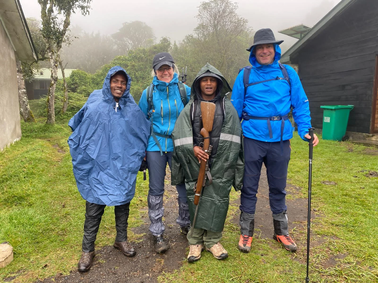 Hikers wearing waterproof rain ponchos standing with mountain guides at a Kilimanjaro trekking camp, Tanzania.