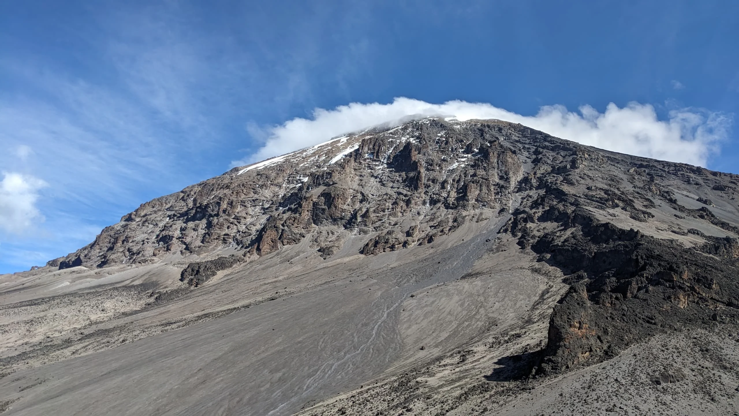 Mount Kilimanjaro's rugged summit rises over volcanic slopes beneath blue skies along the Northern Circuit Route in Tanzania.