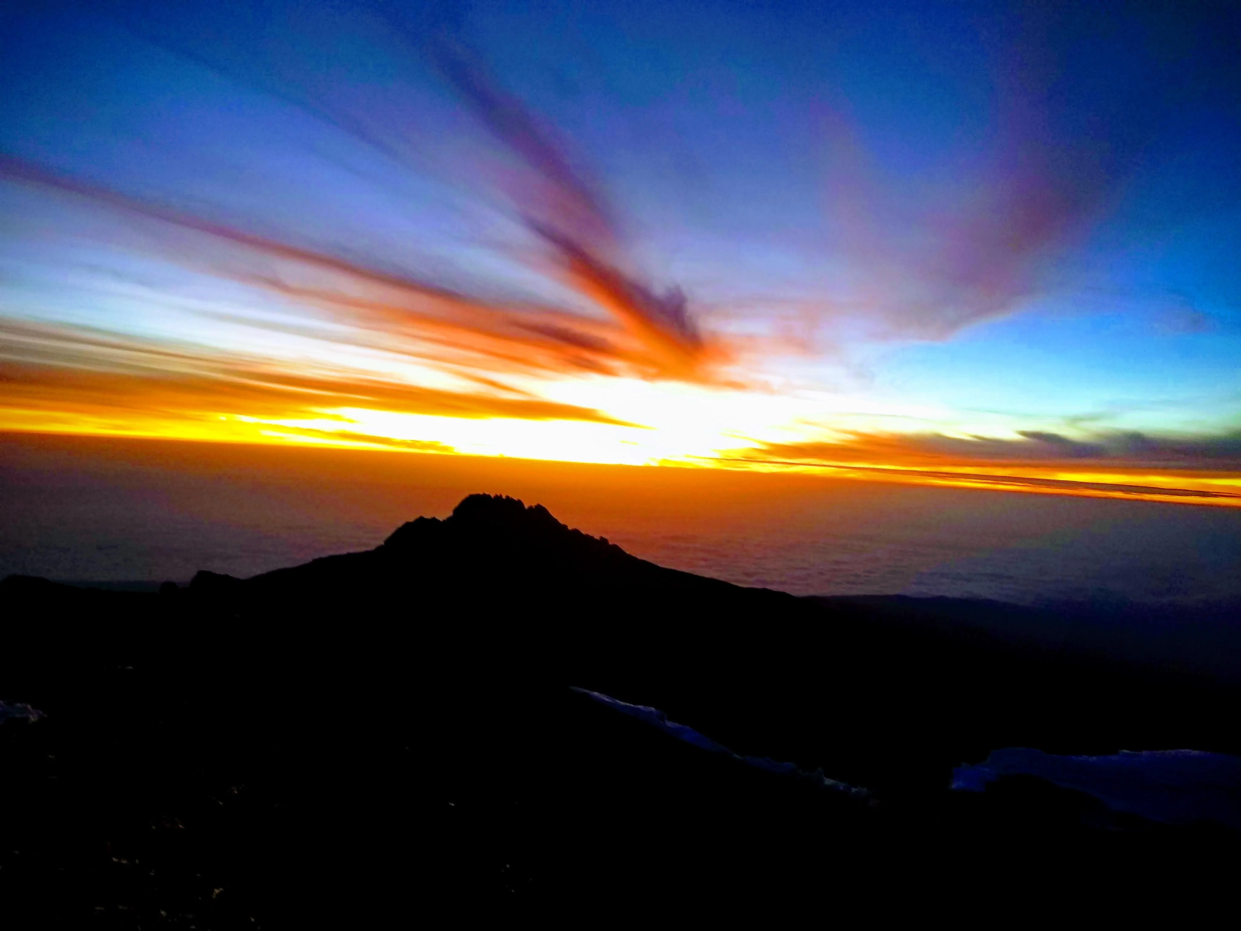 Vibrant orange sunrise sky casting golden light over dark mountain ridges on Mount Kilimanjaro, Tanzania.
