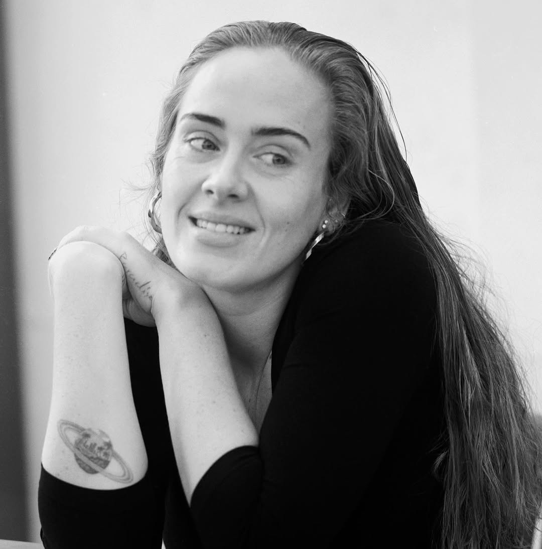 Adele in a black-and-white portrait with a ringed Saturn tattoo visible on her inner forearm