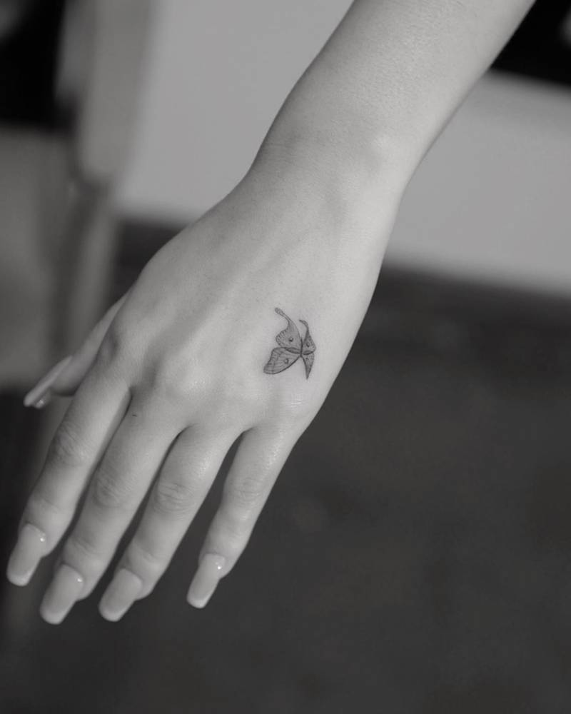 Alexa Demie's left hand showing a small fine-line butterfly tattoo near the thumb