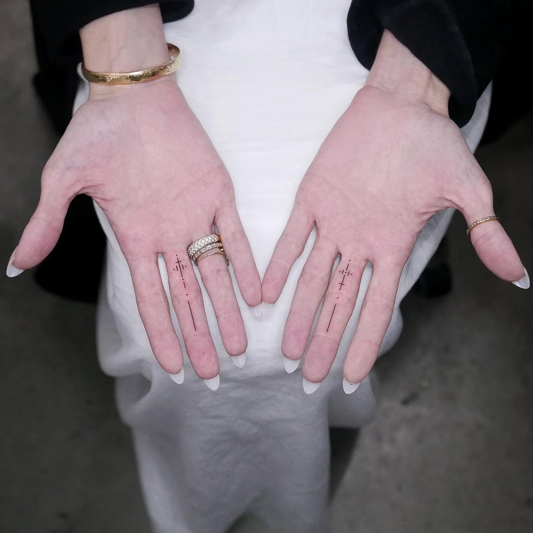 Angelina Jolie holding both palms open to show the paired fine-line geometric dagger tattoos on her middle fingers