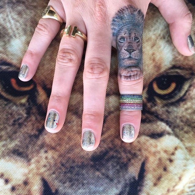 Cara Delevingne’s hand resting on a lion-patterned textile with a detailed lion-head tattoo on the right index finger