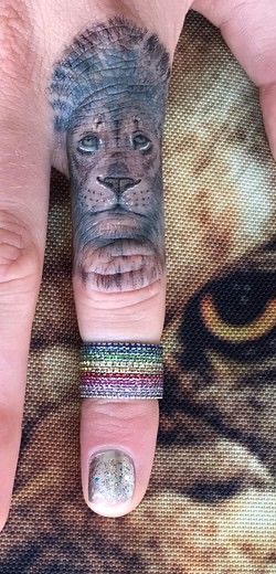 A tight crop of the upright lion face tattoo extending along Cara Delevingne’s right index finger