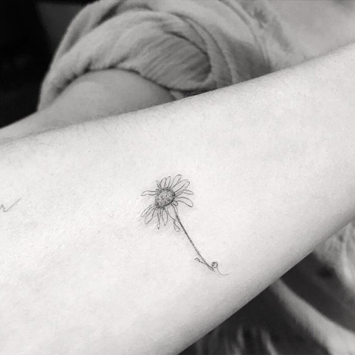 Close black-and-white view of Dakota Johnson’s fine-line wilted daisy tattoo on her right forearm