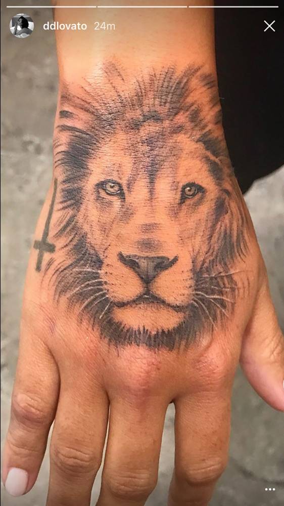 Demi Lovato’s left hand with a black-and-grey forward-facing lion portrait tattoo extending from the wrist toward the knuckles