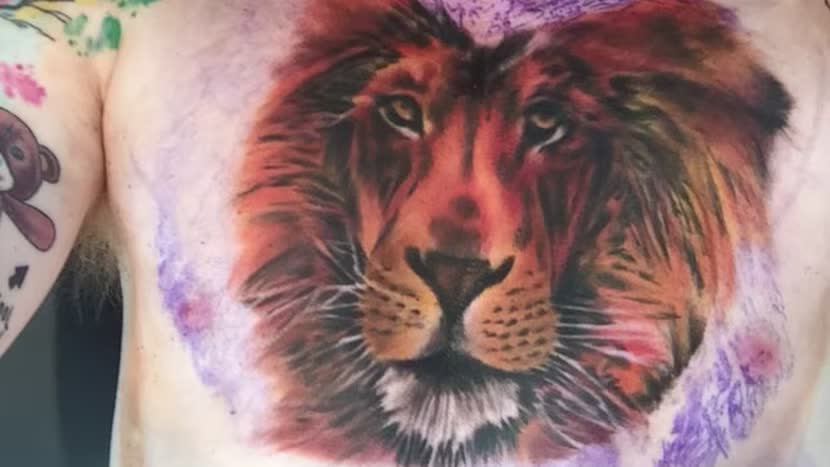 Close source view of Ed Sheeran’s red-orange, black, white, pink, and purple lion head chest tattoo