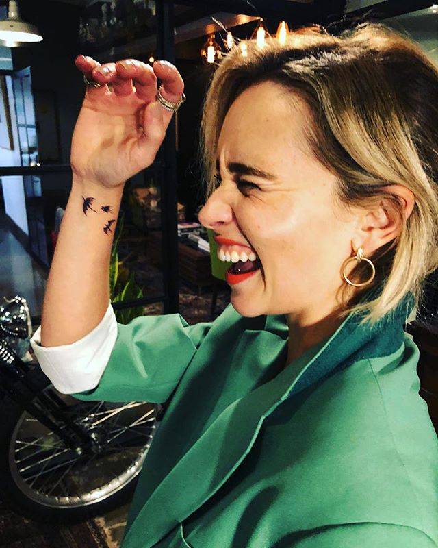 Emilia Clarke raising her right wrist to show three small black flying-dragon tattoos