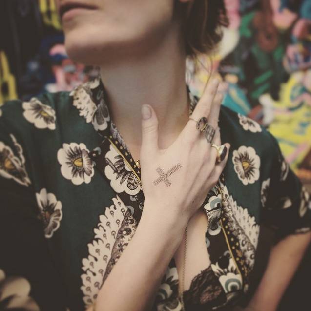 Florence Welch with her right hand near her neck, showing the small ornate cross on the back of her hand