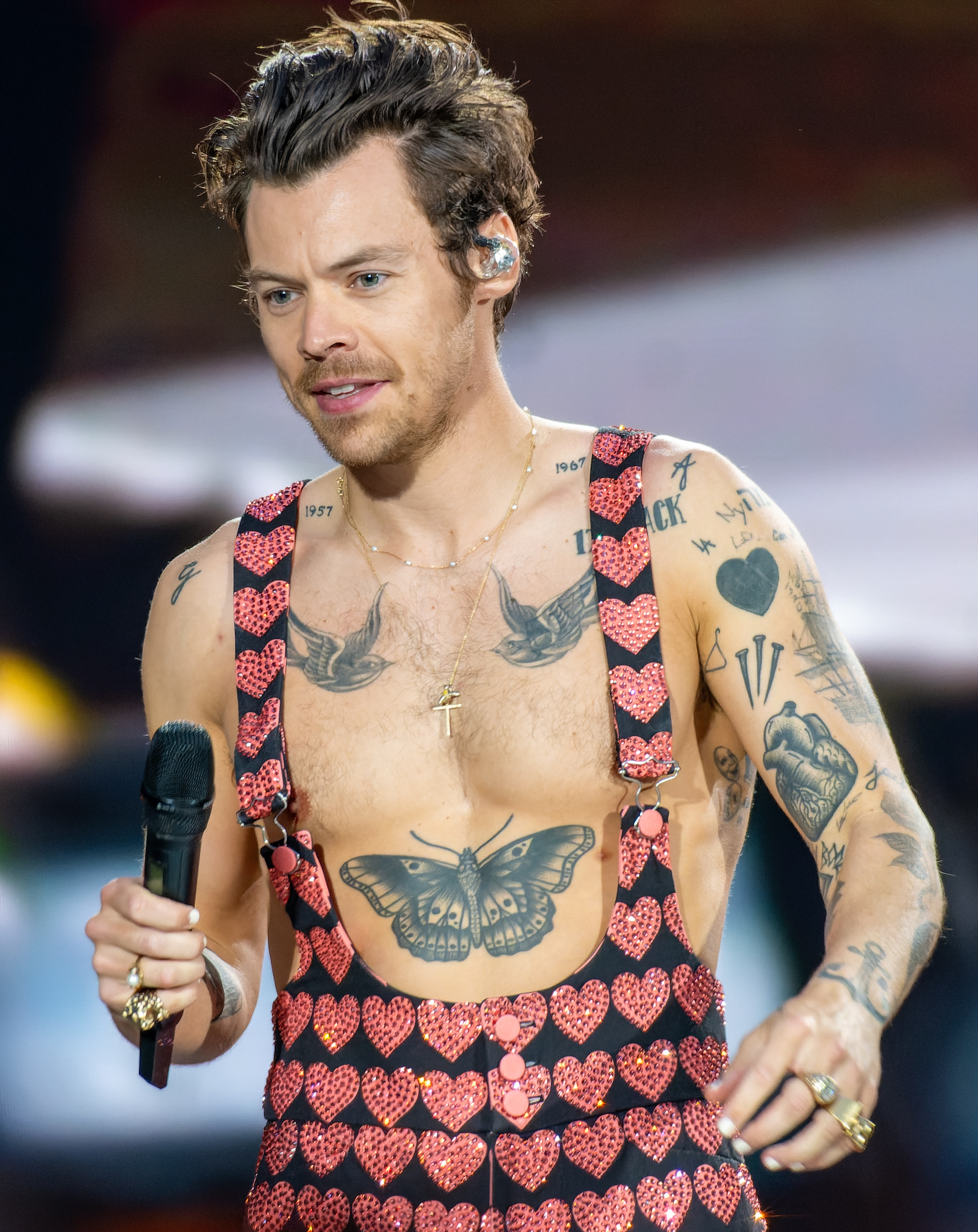 Harry Styles performing at Wembley in 2023 with a filled black heart visible on his left upper arm