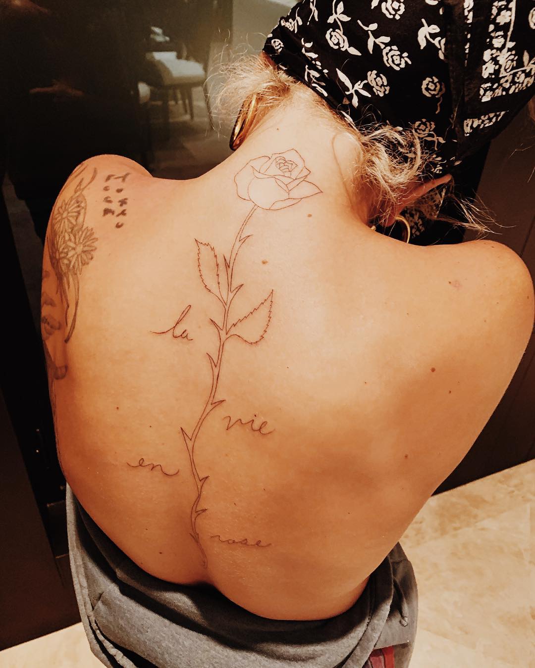 Lady Gaga photographed from behind with a fine-line rose and script tattoo extending down her spine