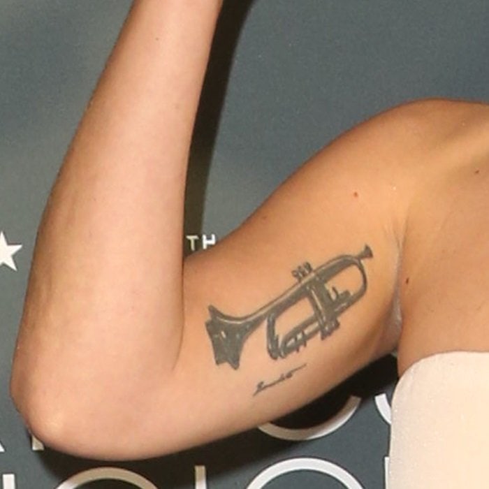 Lady Gaga raising her right arm to show the black trumpet and Benedetto signature tattoo on her inner upper arm