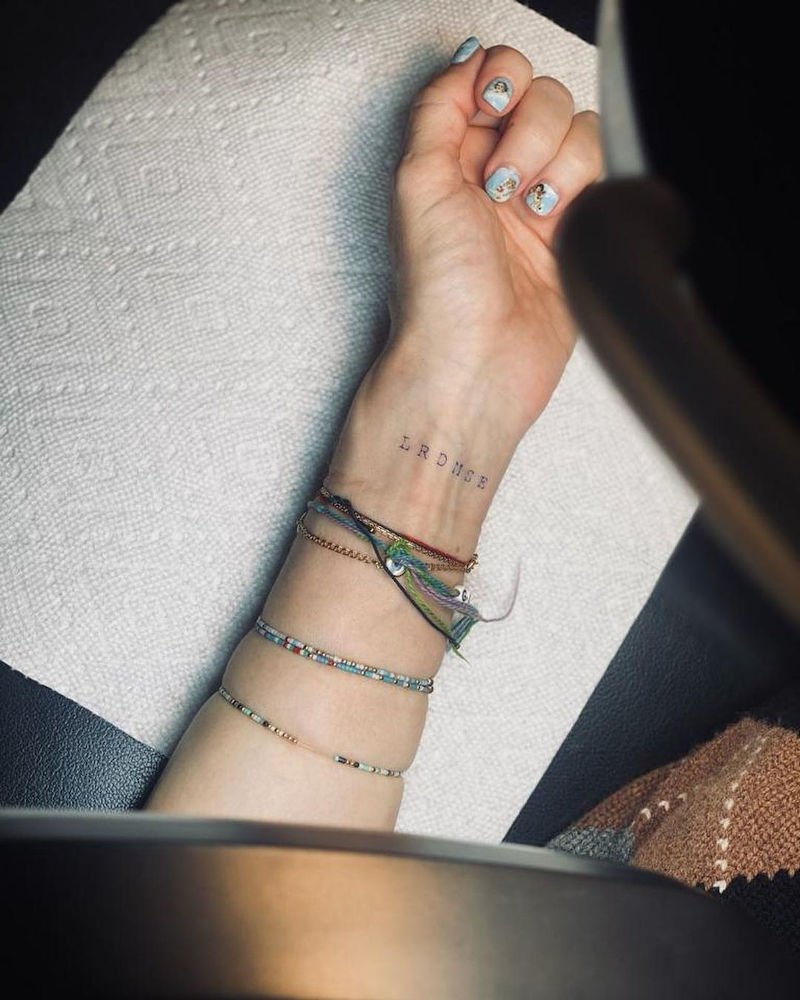 Madonna's inner left wrist shows six small typewriter-style black initials above several bracelets.