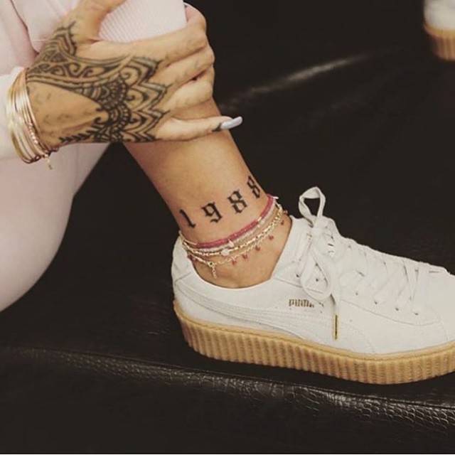 Black Gothic 1988 numerals on Rihanna's right ankle above a white sneaker