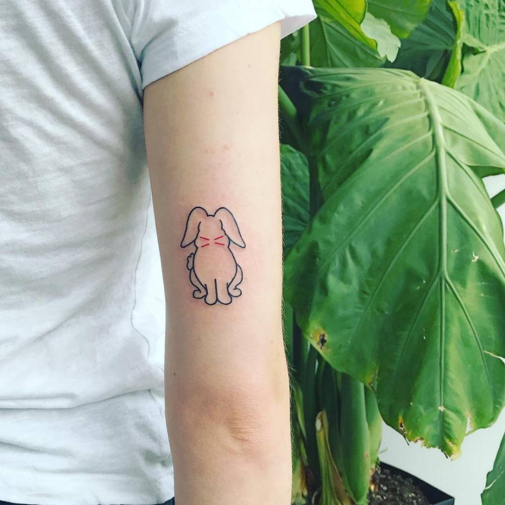 Sophie Turner’s complete rabbit tattoo on the back of her right upper arm, below a white sleeve beside green leaves.