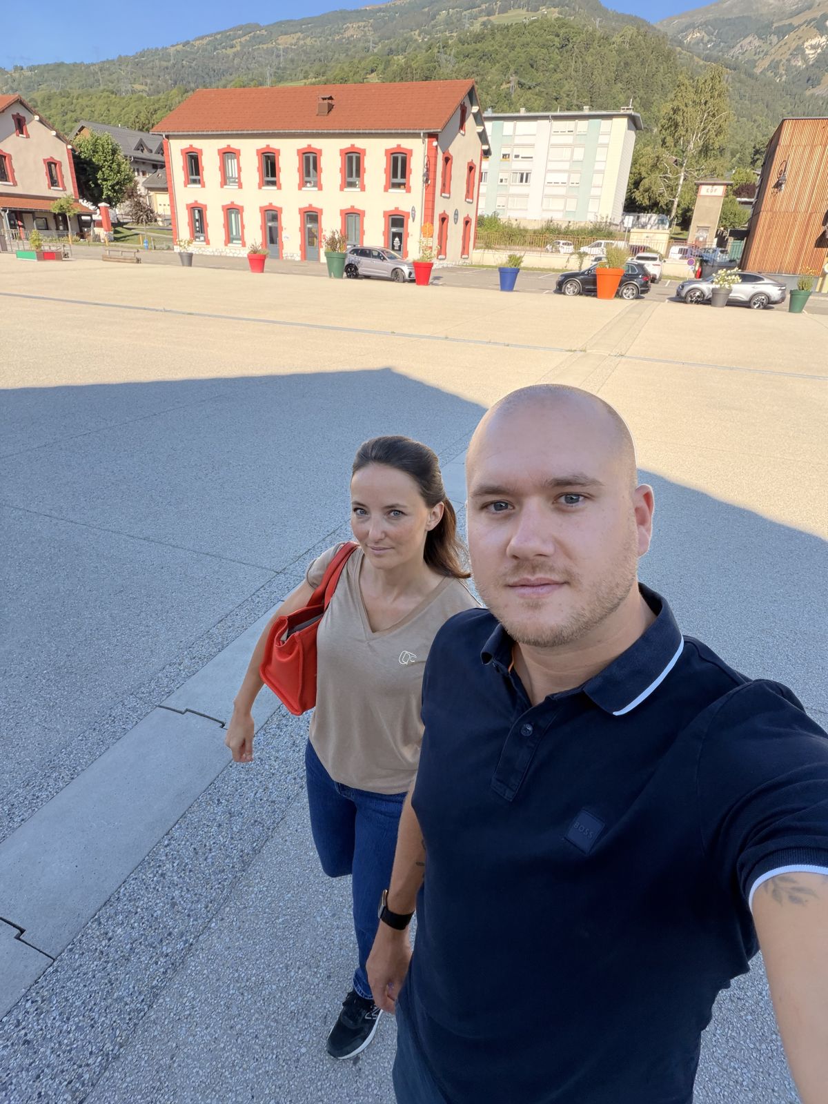 Adrien and Emily in a village square with mountains behind