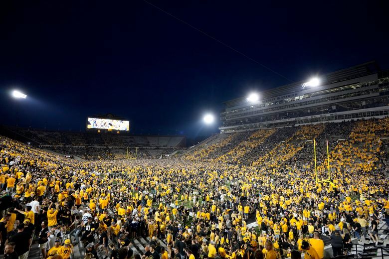 Kinnick Stadium at night filled with Iowa fans storming the field after a football game against Penn State