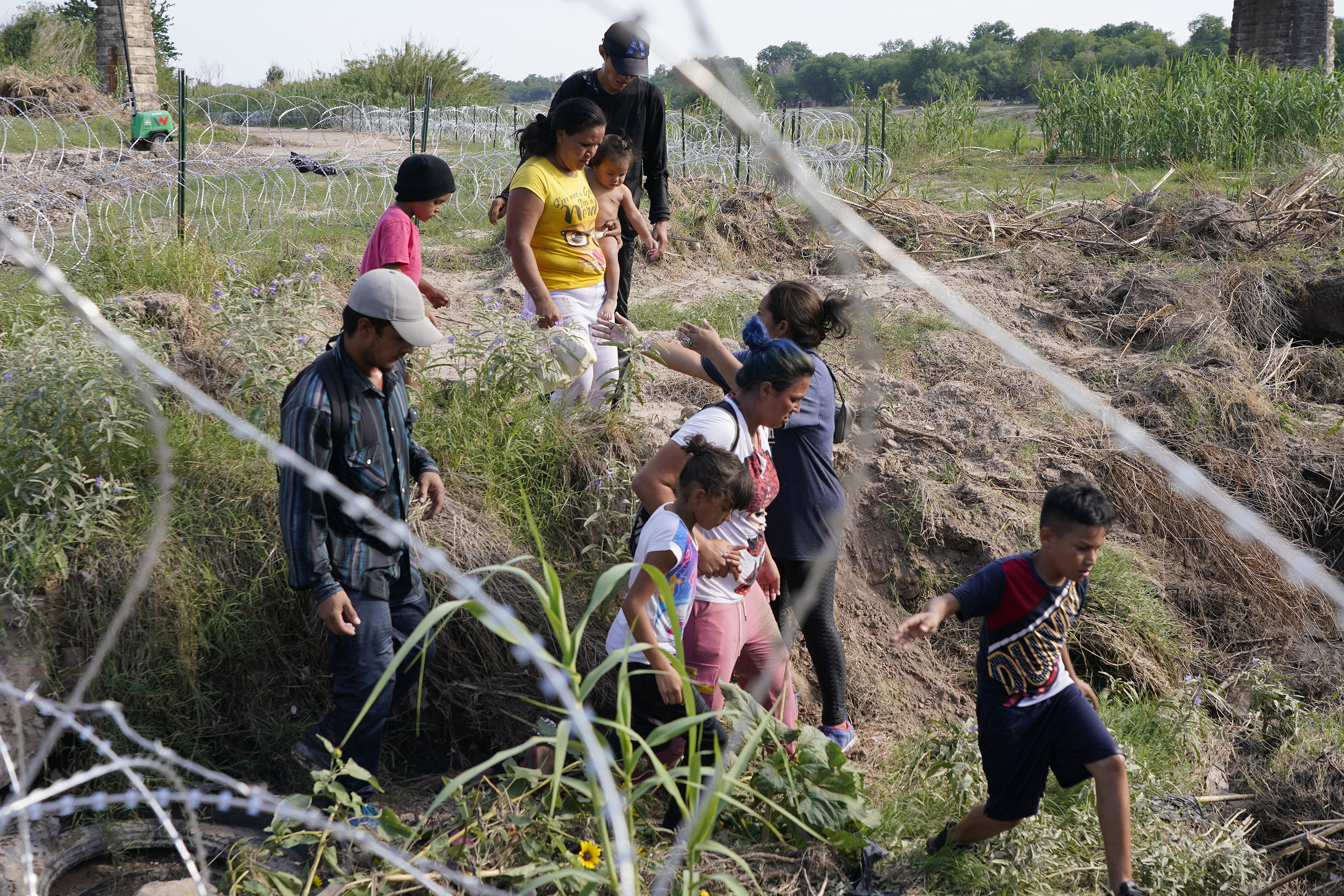 Migrantes, en su mayoría con niños, siguen un sendero a lo largo de la alambrada de concertina donde finalmente serán puestos bajo vigilancia por la Patrulla Fronteriza después de haber cruzado el Río Grande el 27 de mayo de 2022 en Eagle Pass, Texas.