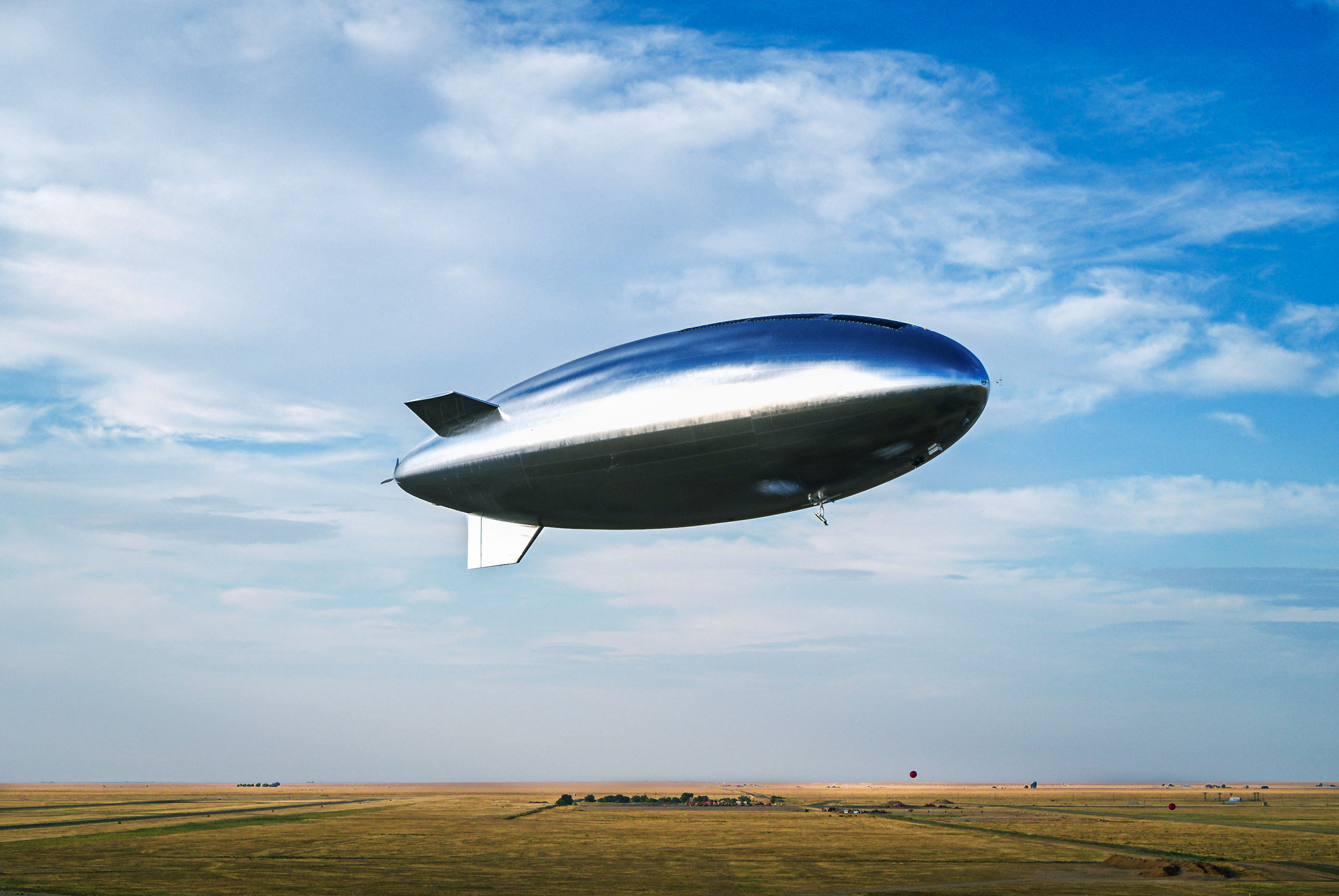 una aeronave plateada similar a un dirigible flotando sobre un campo
