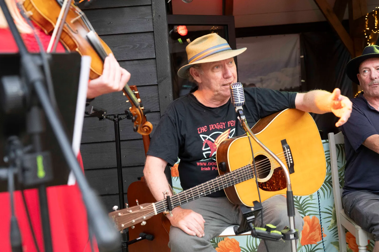 Gitarist in Doggy Few-shirt met strohoed, in gesprek met het publiek