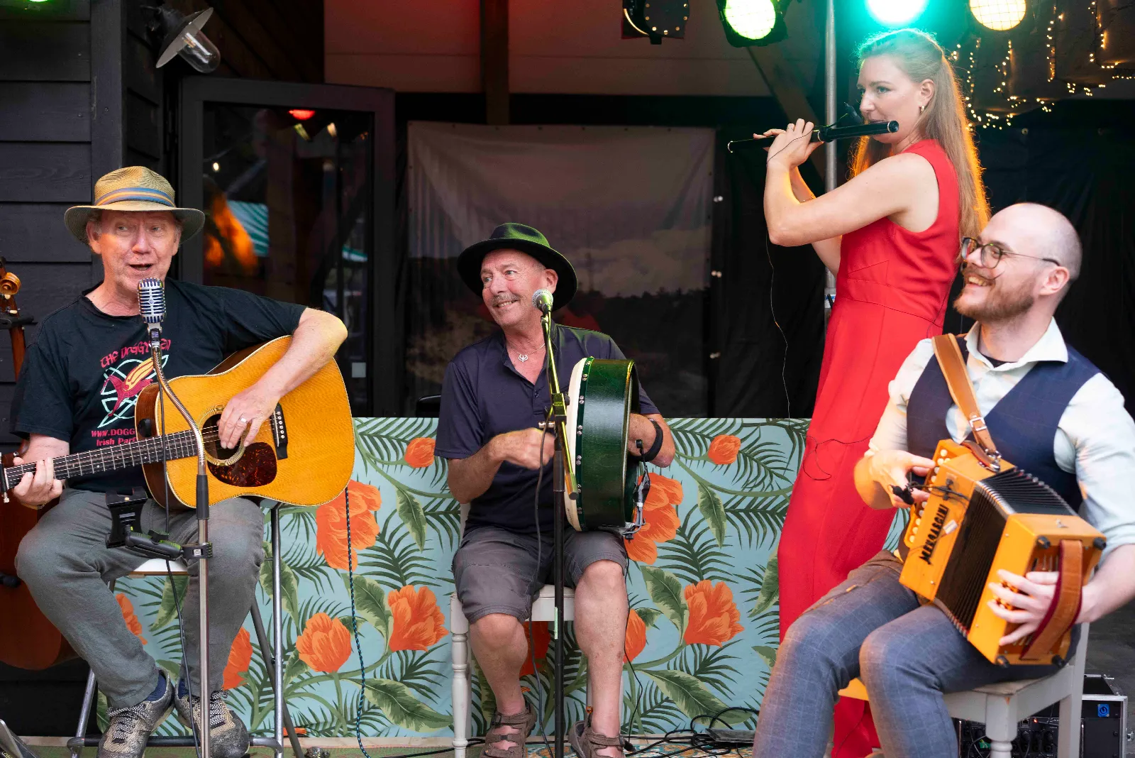 Fluitiste in het rood speelt staand, met gitarist, bodhrán en box naast haar