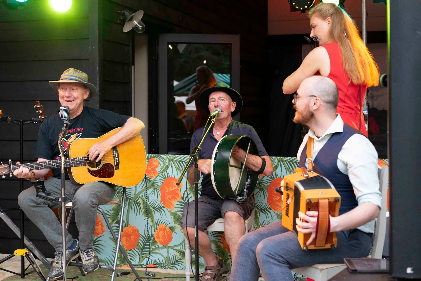Gitarist, bodhránspeler en boxspeler op het podium, de zangeres komt erbij staan
