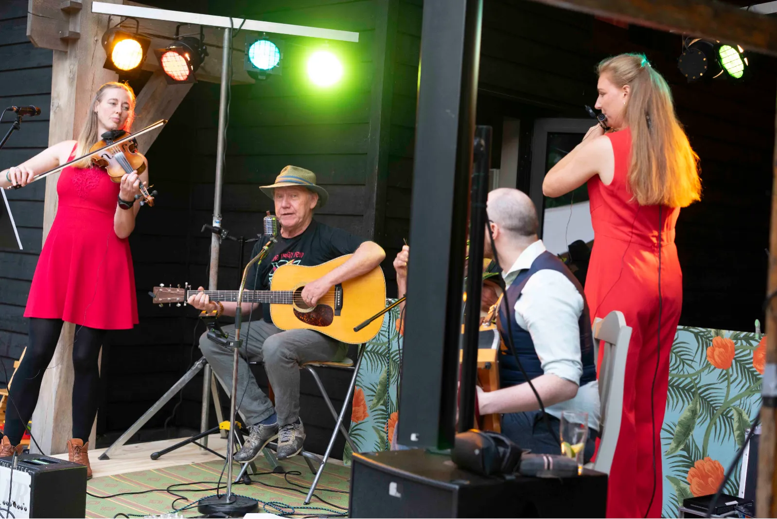 Violiste, gitarist en fluitiste spelen in de avond onder gekleurde lampen