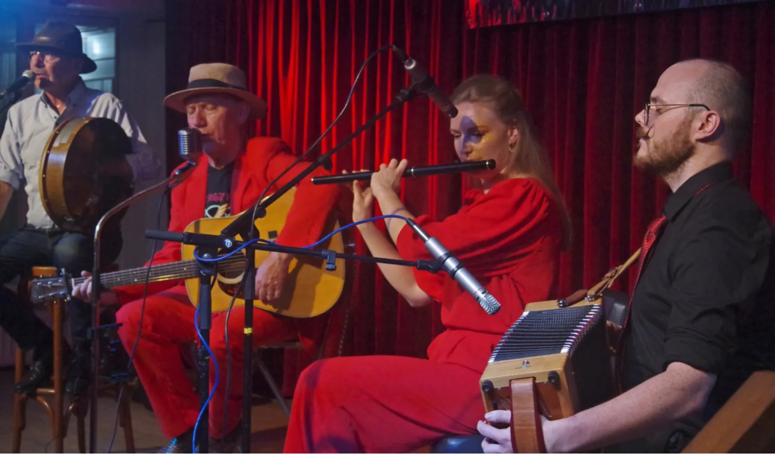 Vier muzikanten dicht op elkaar in rood podiumlicht: fluit, gitaar, bodhrán en box