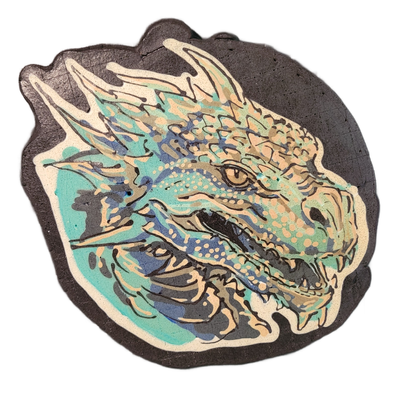 A pancake art piece depicting a dragon head in three-quarter view, facing right, with an open mouth showing teeth, a single visible amber-colored eye, and layered horn and frill structures extending from the top and back of the head. Rendered with fine black outlines and dense detail including dot…