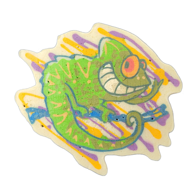 A cartoon gecko rendered in pancake art, shown in profile with a large round eye with a pink iris, an open-mouthed grin showing white teeth, a curled tail, and a bright green scaly body with lighter yellow-green markings along the back and sides. The figure is outlined in bold blue-gray lines, fill…