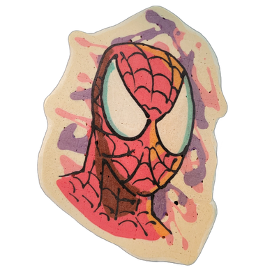 Pancake art depicting a masked superhero face with large white oval eyes outlined in teal, a red costume covered in a black web-line pattern, and orange-yellow shading along the right side of the face. Bold black outlines define the features, with fill areas in deep red and orange batter; pink and…