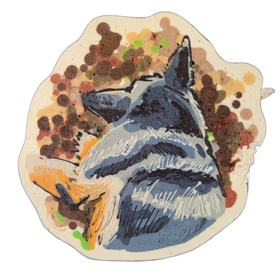 Pancake art depicting a blue-gray dog or wolf-like animal shown from the chest up, head tilted upward and slightly to the left, with pointed ears, a light-colored muzzle, and layered fur detail across the chest and neck area. The subject is rendered with bold black outlines and blue-gray fill batte…