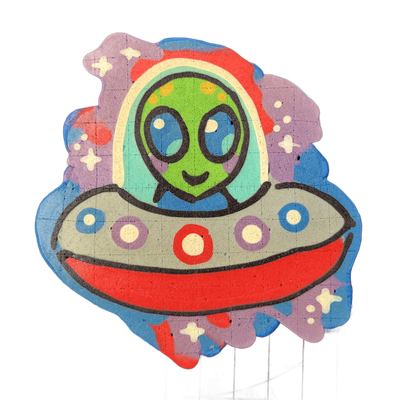 Pancake art depicting Trav, a green-skinned cartoon alien with large dark oval eyes and a small curved mouth, shown from the chest up inside a domed flying saucer cockpit with a rainbow-arched canopy; the saucer body is gray with a red underside and rows of circular lights in blue, purple, and whit…